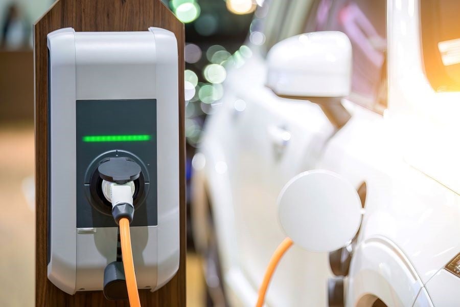 An electric vehicle charging station with an orange cable plugged into a white car. Green indicator lights are on.