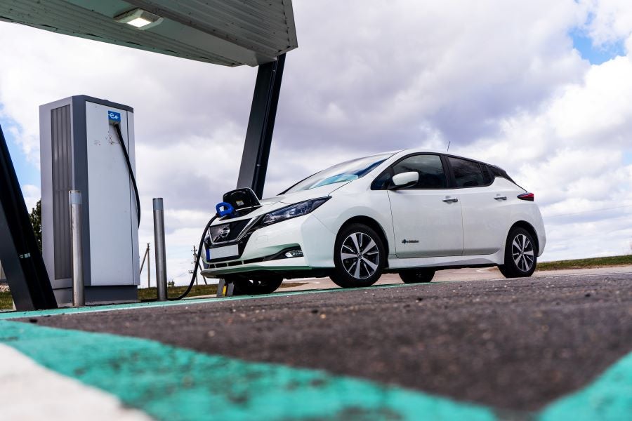 A electric car charging at a station under a cloudy sky.