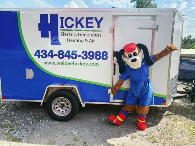 A person in a dog mascot costume posing next to a white trailer with large 'HICKEY' logo and contact info.