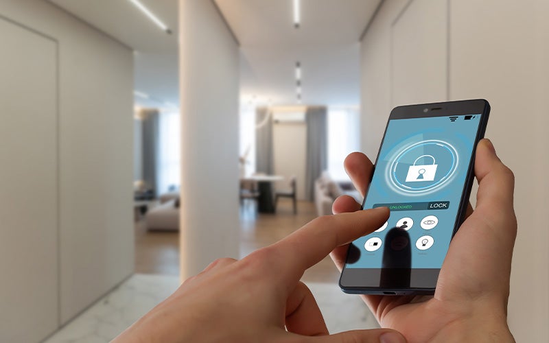 Hands holding a smartphone displaying a smart home app with a padlock icon on the screen