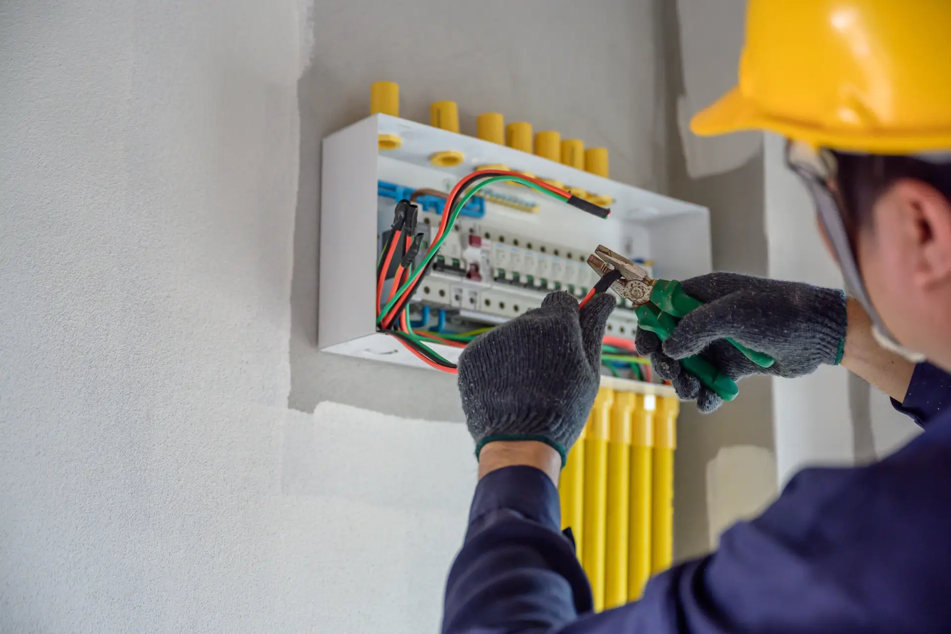 An electrician in a hard hat and gloves works on a residential circuit 