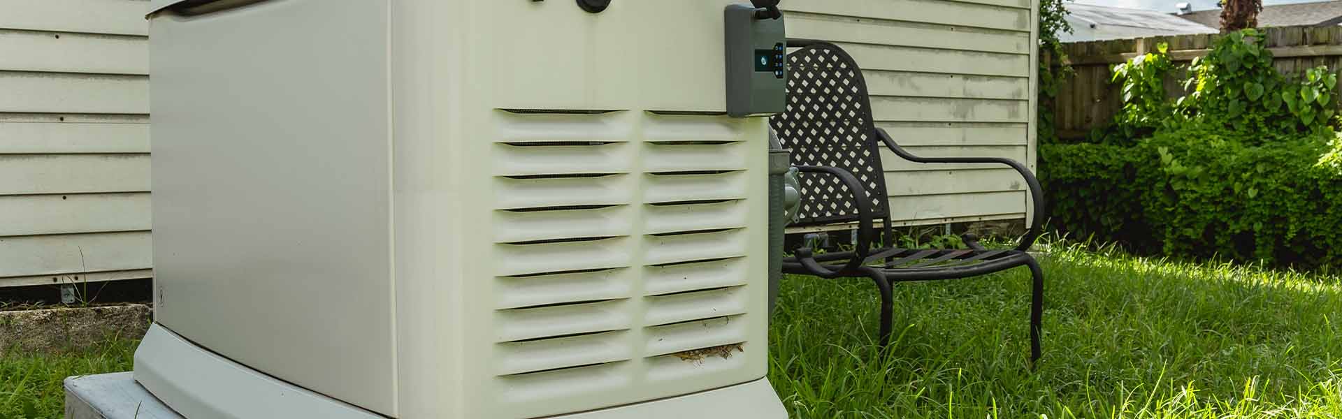 A generator sits next to a dilapidated house and overgrown greenery.
