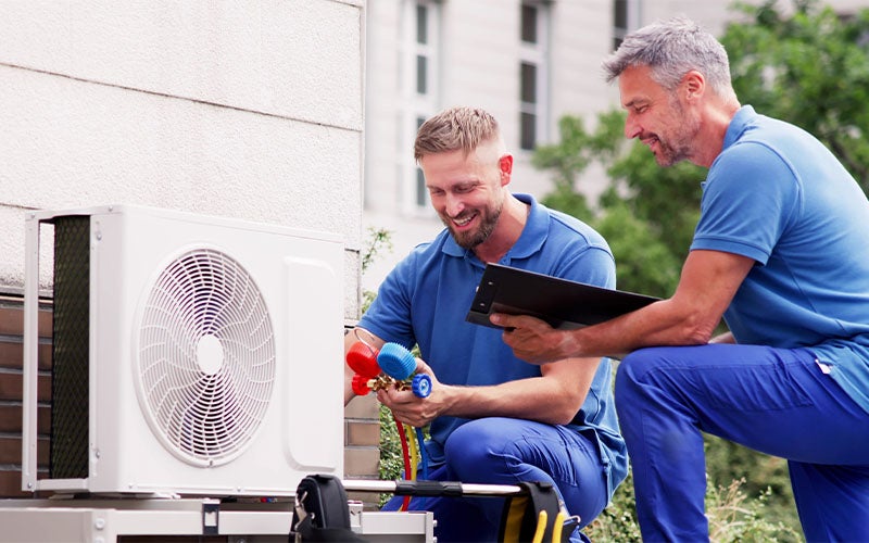 Two repairing an outdoor AC unit.