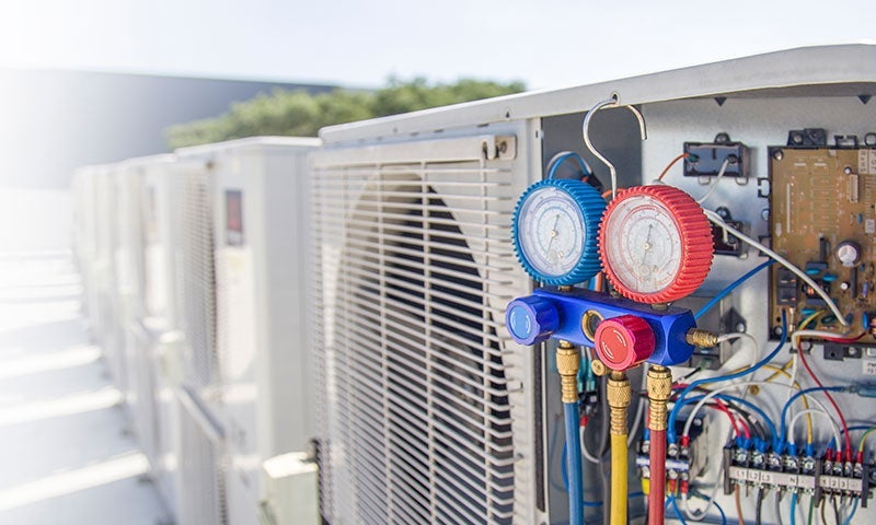 A row of AC units, one with an open panel showing wires and a pressure gauge set.