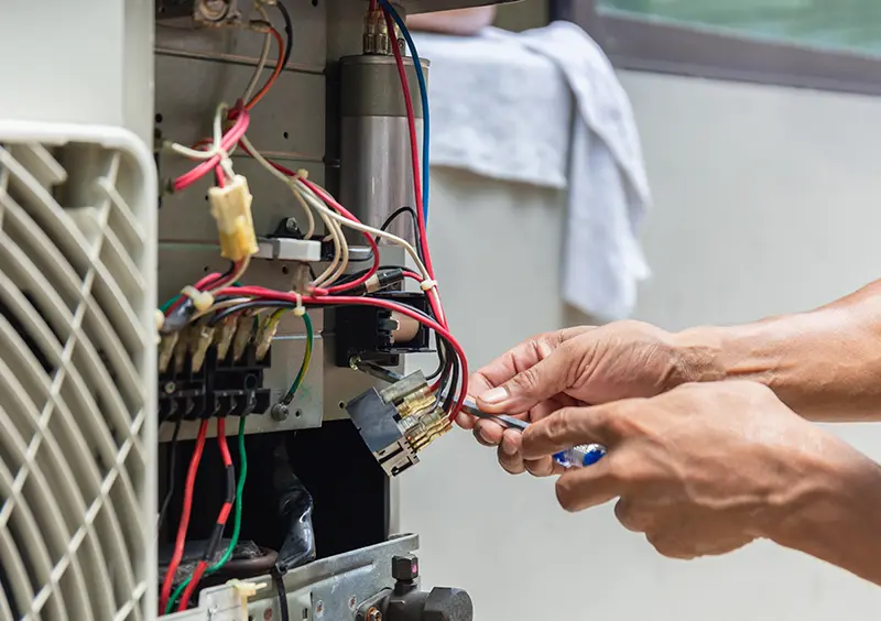 An electrician in a hard hat and gloves works on a residential circuit 