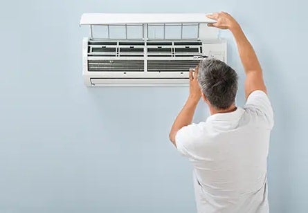 A man wearing a white t-shirt and with gray hair is installing or repairing the indoor unit of an air conditioner.