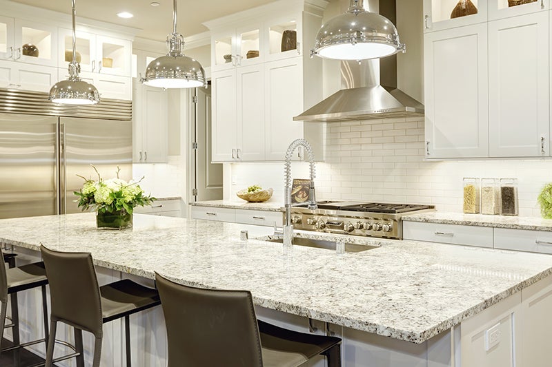 A bright, modern kitchen features white cabinets, stainless steel appliances, and mottled white granite countertops.