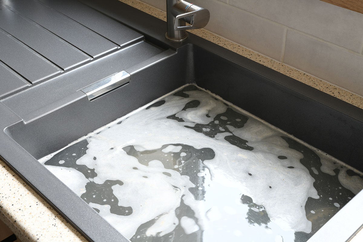 A kitchen sink is filled with dirty, soapy water. A faucet is visible to the left.
