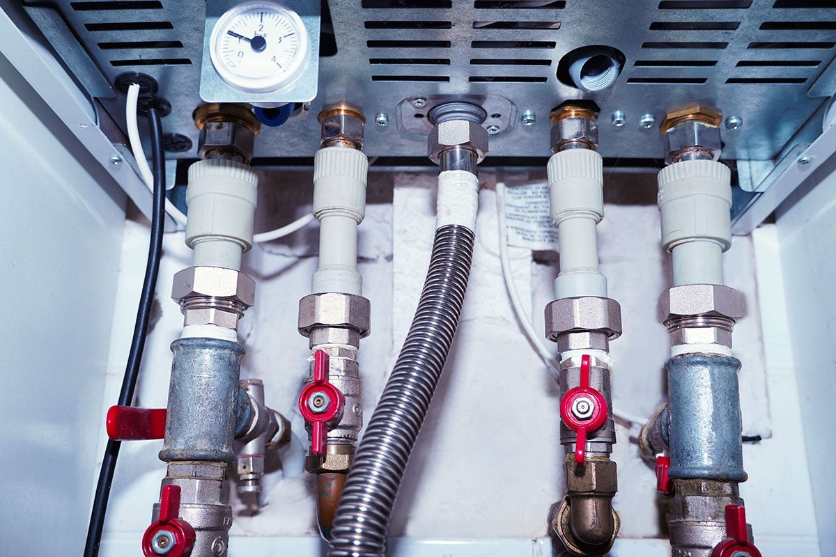 Close-up of a water heater's pipes with red valves, pressure gauge, and electrical wires.