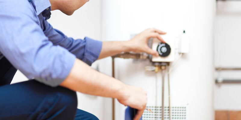 A person in a blue shirt adjusts the temperature knob of a white water heater.